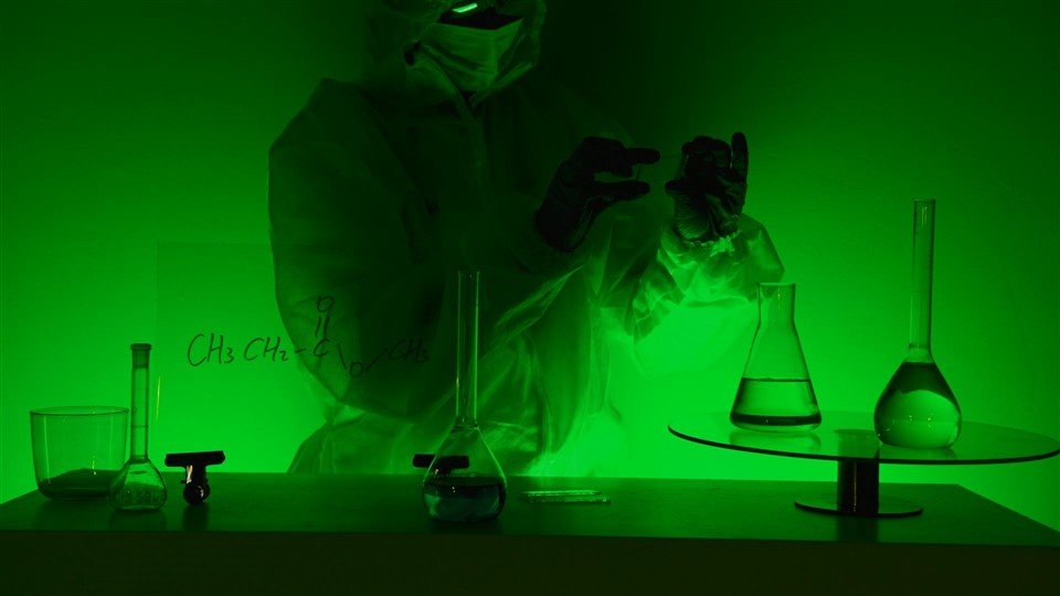 Personne en combinaison de protection dans un laboratoire à lumière verte – métaphore d’un environnement de travail toxique invisible