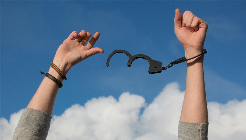 Photo représentant les bras en l'air d'une personne qui se libère de ses menottes, pour illustrer l'expression citée dans l'article : nommer les causes du travail toxique, c'est briser l’illusion qu'on n'a pas le choix