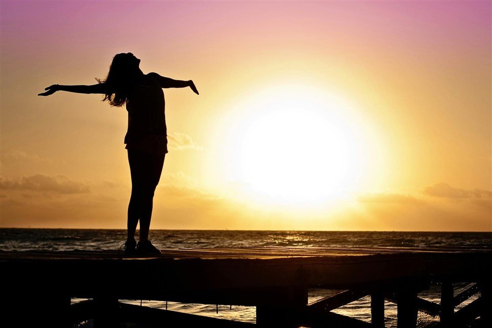 Silhouette d’une femme sur un ponton, bras ouverts vers le coucher de soleil, symbole de liberté après un manager toxique.
