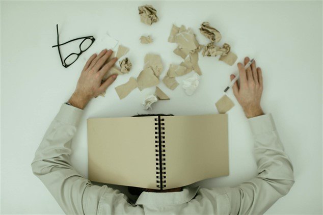Photo vue de haut d’un collaborateur épuisé, la tête sur son bureau recouverte d’un carnet de notes, avec des feuilles froissées et des mouchoirs, illustrant le stress et l’impact d’un manager toxique sur la santé au travail.