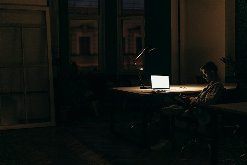 Employé travaillant tard le soir dans un bureau sombre, ordinateur portable allumé, illustrant les heures supplémentaires quand on a trop de travail