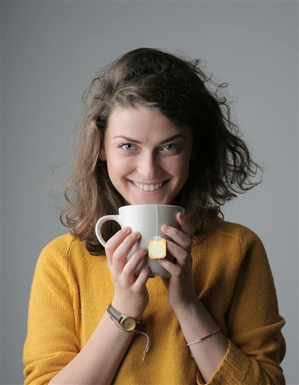 photo d'une femme tenant une tasse de thé qui sourit malicieusement en regardant droit dans l'objectif pour illustrer une des signes de collègue toxique au travail, la critique sous couvert d'humour