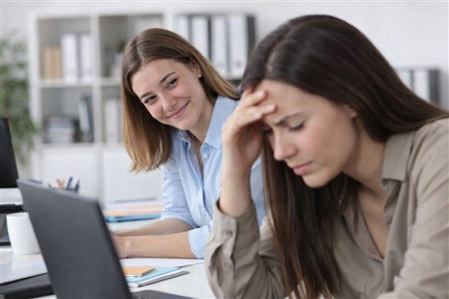 Collègue jalouse au travail souriant pendant que sa collègue rencontre des difficultés
